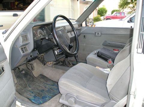 1986 Toyota Hilux - The interior of a white Toyota pickup truck, with a red pickup truck visible through the window.
