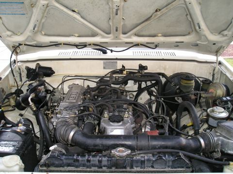 1986 Toyota Hilux - The engine bay of a white 1986 Toyota Hilux shows its V6 engine and associated components.