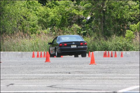 2001 Mercury Grand Marquis - A black sedan navigates a course marked by orange cones on a paved surface, with trees and vegetation in the background.