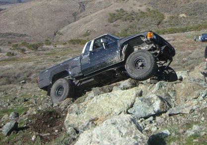 1985 Toyota Hilux - This 1985 Toyota Hilux is shown off-roading on a rocky incline, demonstrating its capability on challenging terrain.