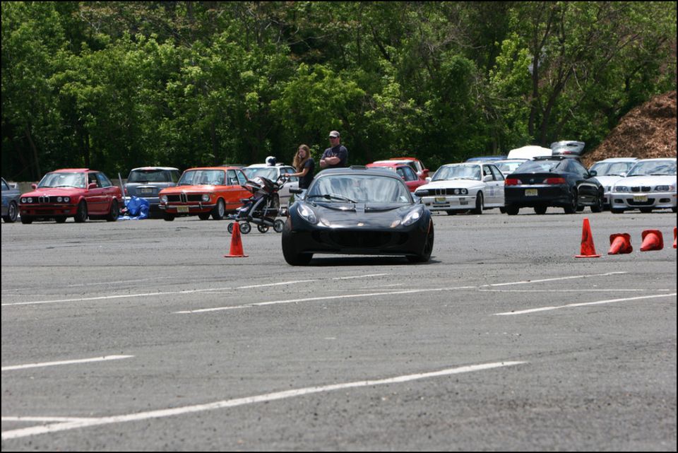 Black sports car in foreground, with other cars and people in background at an event