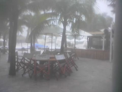 1989 Ford Bronco - A beachside cafe is battered by a storm, with tables and chairs exposed to the elements and rough seas visible.
