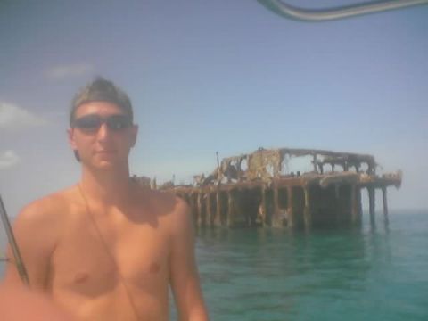 1989 Ford Bronco - A man stands in front of a large, rusted shipwreck in the clear blue ocean.