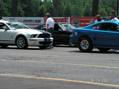 1988 Ford Mustang - Three Mustangs are lined up at a drag strip, with spectators in the background.