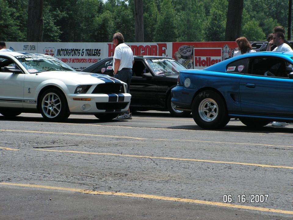 White Mustang GT500 and blue Mustang at drag strip. Black car behind white one