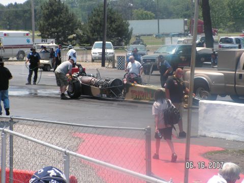1988 Ford Mustang - Dragster with jet engine on track, with support vehicles and spectators present.