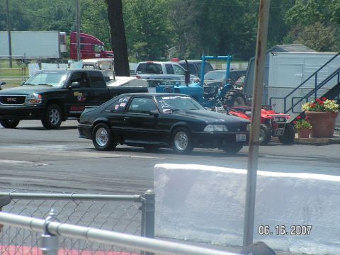 1988 Ford Mustang - A black 1988 Ford Mustang hatchback is seen on the drag strip with other vehicles in the background.