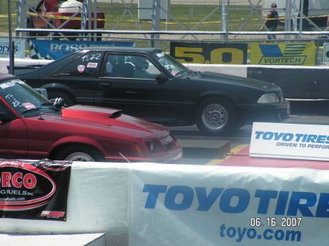 1988 Ford Mustang - A black 1988 Ford Mustang coupe is seen on the drag strip next to a red car.