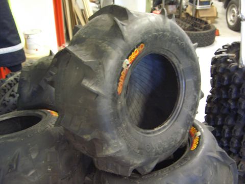 1974 Ford Bronco - Several large off-road tires are stacked, with one tire clearly showing the brand name SAND RECKO.