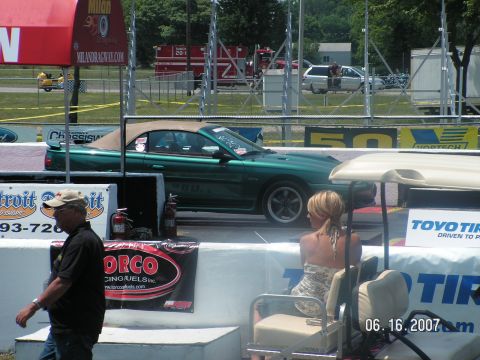 1988 Ford Mustang - A green convertible Mustang is staged at a drag strip, with spectators and a golf cart visible.