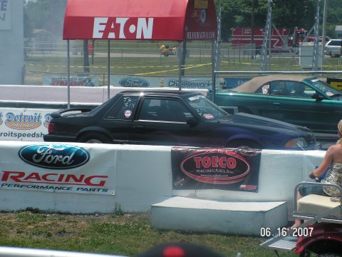 1988 Ford Mustang - A black Ford Mustang is on a drag strip next to a green convertible.