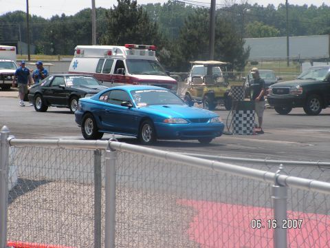 1988 Ford Mustang - A blue coupe is positioned on a drag strip, with an ambulance and other vehicles visible in the background.