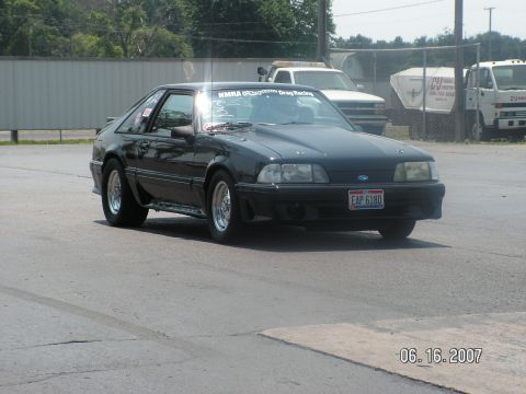 1988 Ford Mustang - A black 1988 Ford Mustang hatchback is shown from the front-three-quarter view on a sunny day.