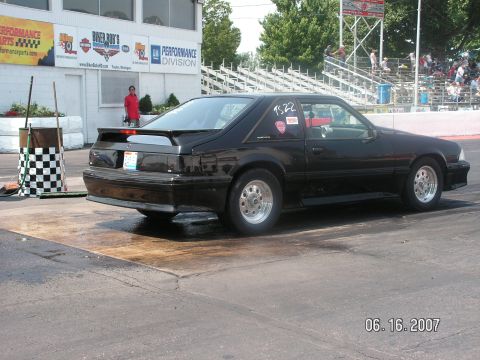 1988 Ford Mustang - A black coupe with a spoiler and racing decals sits on a wet track.
