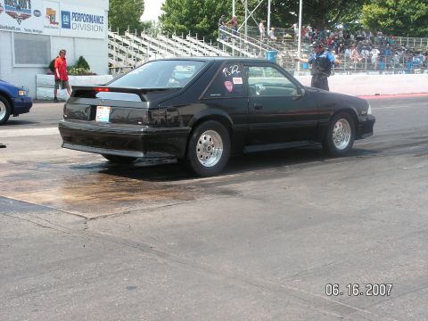 1988 Ford Mustang - A black 1988 Ford Mustang coupe is seen on the drag strip, with spectators in the background.
