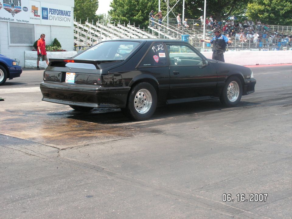 Black 1988 Ford Mustang coupe drag car, rear 3/4 view, on track