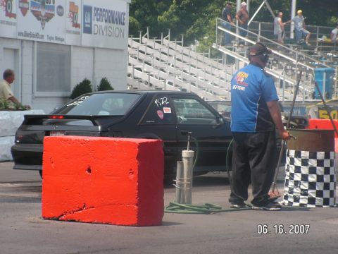 1988 Ford Mustang - A black 1988 Ford Mustang is seen at a drag strip, with a race official standing nearby.