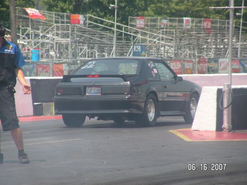 1988 Ford Mustang - A black coupe drag car with a spoiler and racing slicks is seen from the rear at a drag strip.
