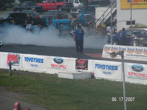 1988 Ford Mustang - A blue tractor performs a burnout at a drag strip event, creating a large cloud of smoke.