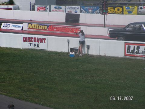 1988 Ford Mustang - A black sedan is on the drag strip at Milan Dragway, with a person standing nearby.