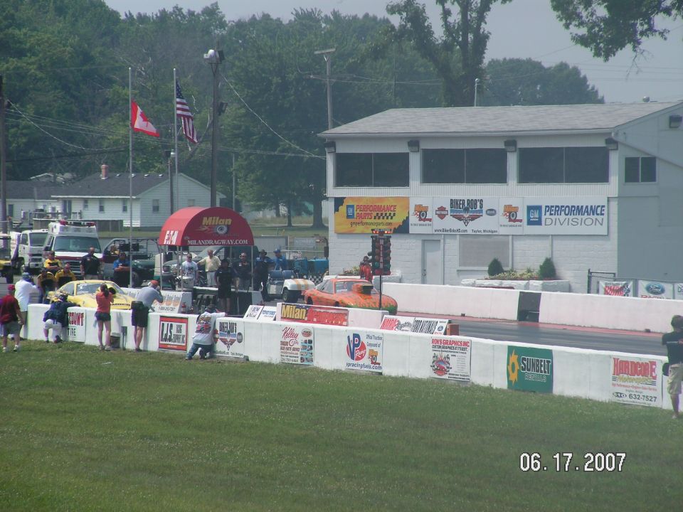 Drag strip scene with multiple race cars, spectators, and buildings. Date stamp reads 06 17 2007