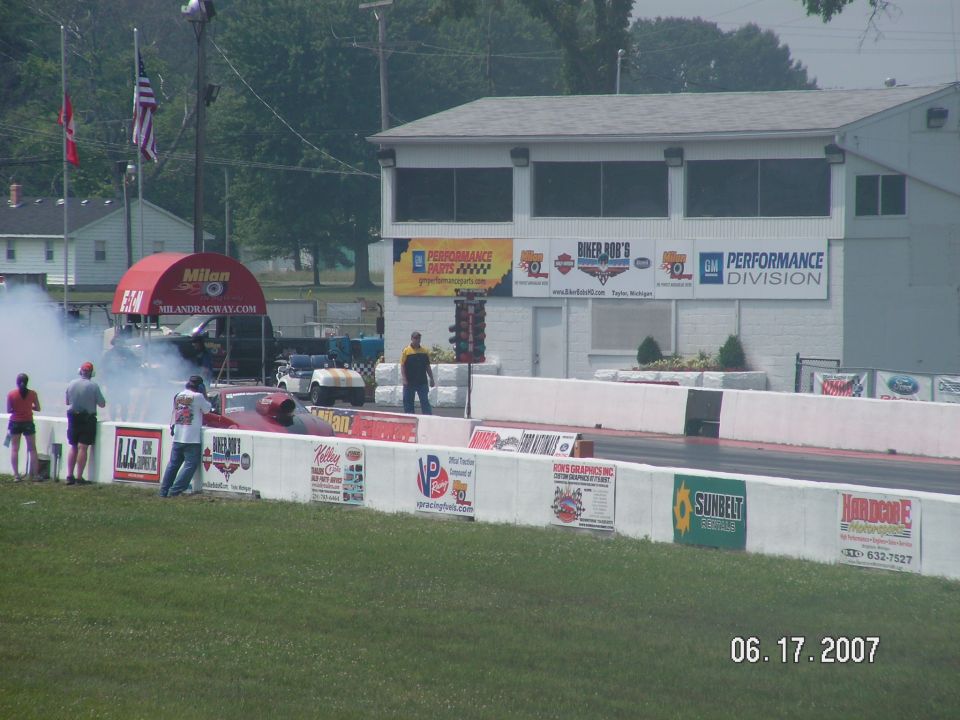drag car doing a burnout at Milan Dragway, with spectators and buildings in background