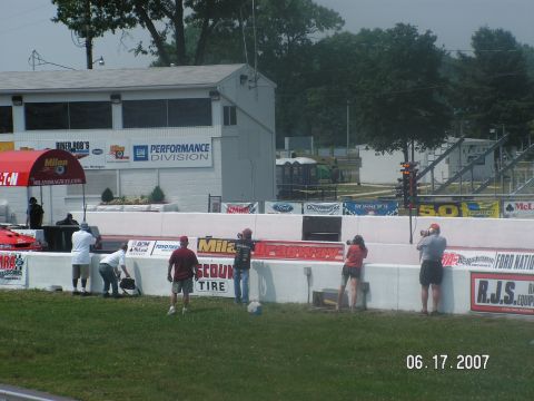 1988 Ford Mustang - A red race car is visible at a drag strip with spectators and buildings in the background.