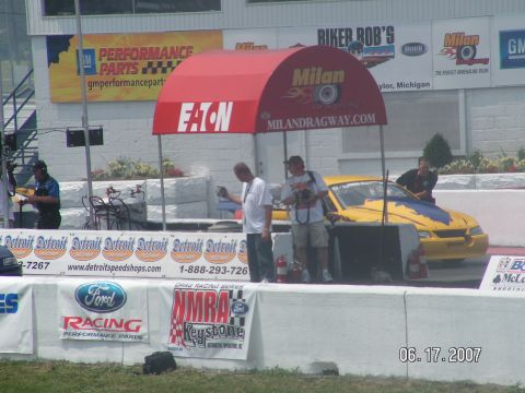 1988 Ford Mustang - A yellow drag car is prepared for a race at Milan Dragway, with spectators and crew members around.