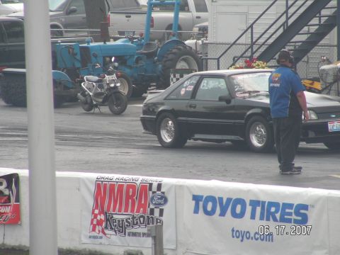 1988 Ford Mustang - A black 1988 Ford Mustang is seen on the drag strip with a person standing nearby.