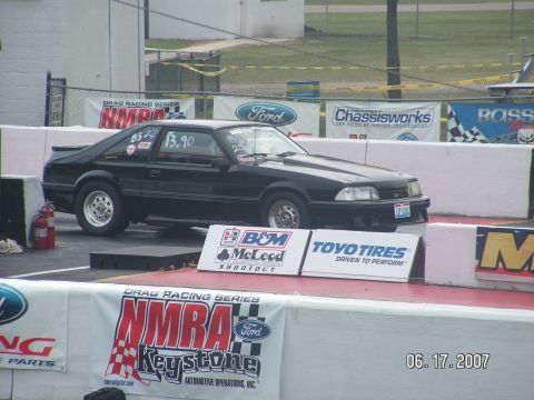1988 Ford Mustang - A black 1988 Ford Mustang drag car is staged on the starting line at a drag racing event.