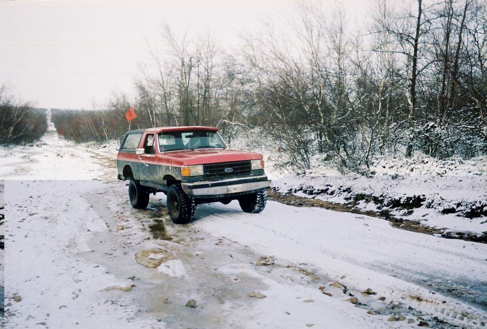 Lifted red and black Ford Bronco with orange flag on a snowy muddy trail