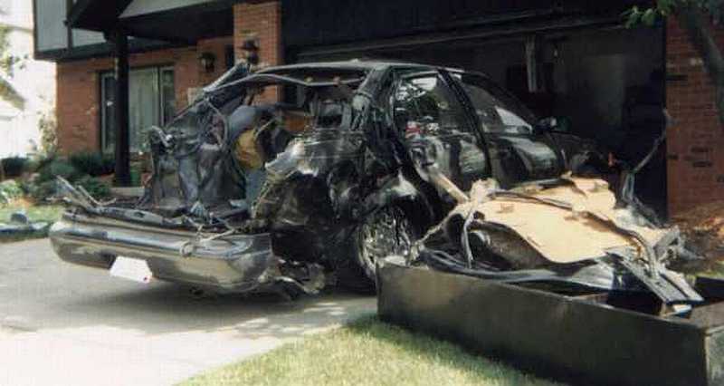 Dark sedan with roof and rear body blown apart parked in a driveway