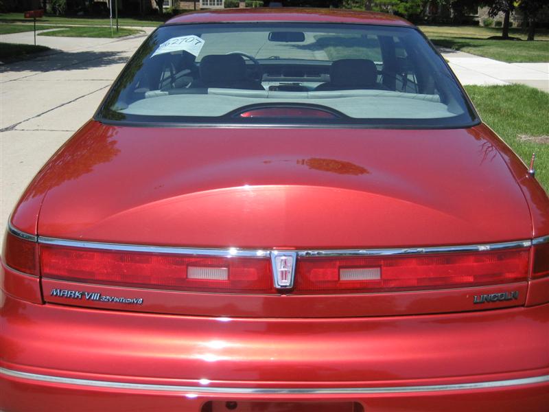 Rear view of a red 1996 Lincoln Mark VIII. Taillights span the rear with a Lincoln emblem in the center