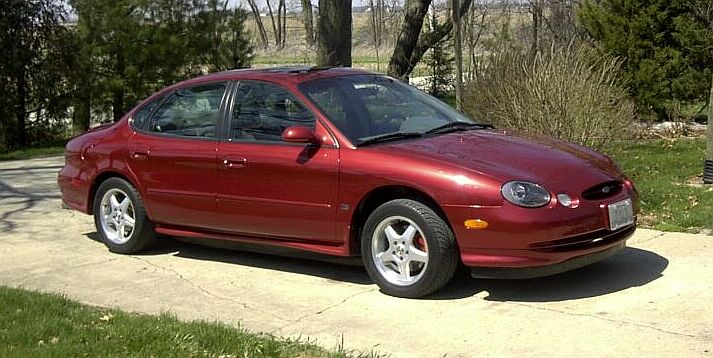 Dark red Ford Taurus sedan with alloy wheels parked on a driveway, passenger-side front three-quarter view