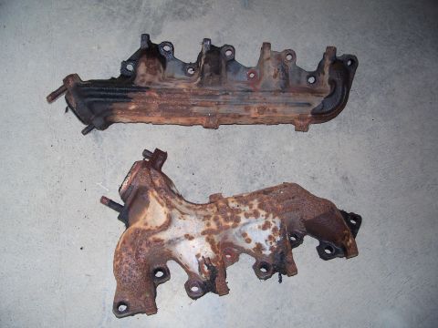 1979 Ford F-150 - Two heavily rusted exhaust manifolds are shown, likely removed from a vehicle for repair or replacement.