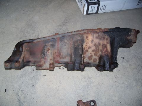 1979 Ford F-150 - Rusted exhaust manifold, likely for an older truck or car, resting on a concrete surface.