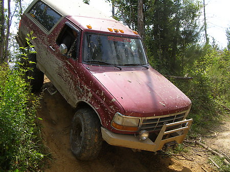 1995 Ford Bronco - A mud-splattered maroon full-size Ford Bronco with a white removable hardtop and cab-roof clearance lights climbs a rutted dirt trail throu…