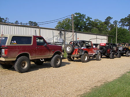 1995 Ford Bronco - A line of off-road vehicles, including a Ford Bronco and multiple Jeeps, are parked outside a building.