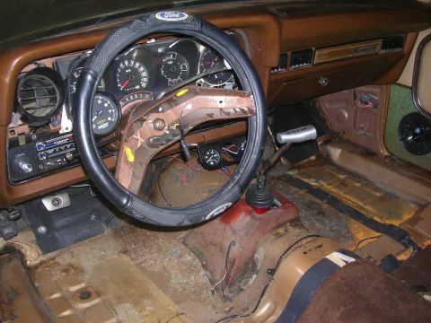 1975 Ford Ranchero - The interior of a 1975 Ford Ranchero shows a brown dashboard, worn seats, and a manual transmission shifter.