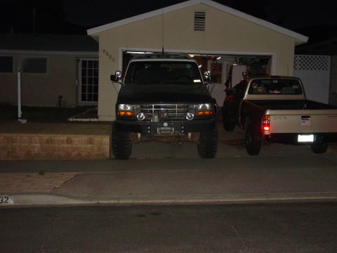 1994 Ford Bronco - Night front view of a lifted dark green Ford Bronco parked in a residential driveway, wearing a tubular front bumper with mounted winch, fo…
