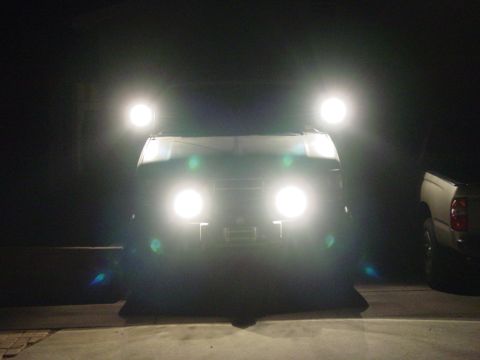 1994 Ford Bronco - A vehicle's front is illuminated by four bright auxiliary lights, with another truck parked nearby.