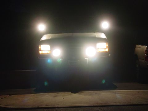 1994 Ford Bronco - 1992 Ford Bronco front end illuminated by headlights and spotlights. Another vehicle is parked nearby.