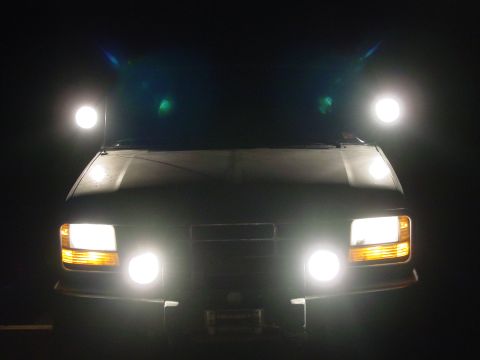 1994 Ford Bronco - The vehicle's front end is illuminated by its headlights and additional driving lights.