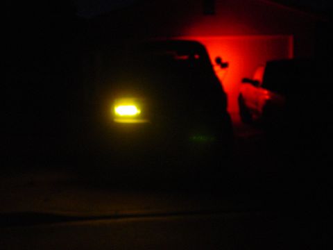 1994 Ford Bronco - Two vehicles are visible in the dark, one with a yellow headlight and the other with a red taillight.