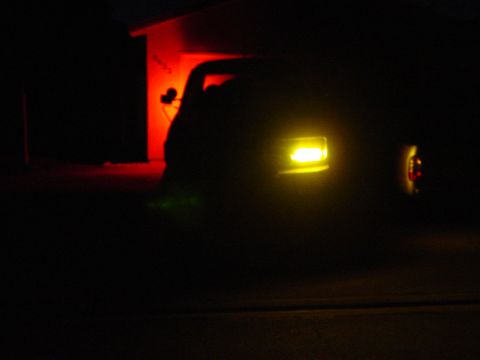 1994 Ford Bronco - A vehicle's yellow headlight is illuminated at night, with a red light visible in the background.