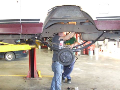 1990 Ford Bronco - Two mechanics are working on the rear leaf springs of a maroon and white Ford Bronco lifted on a service bay lift.