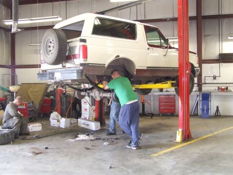 1990 Ford Bronco - Mechanics are working on the undercarriage of a 1990 Ford Bronco on a lift in a garage.