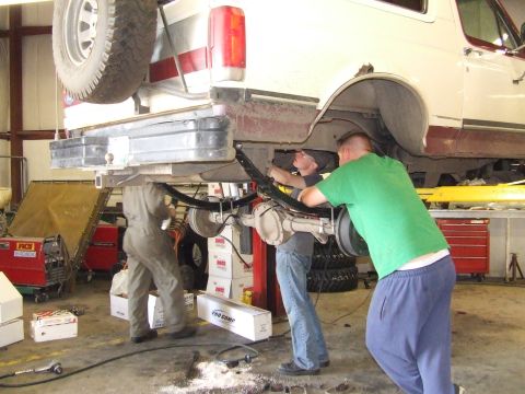 1990 Ford Bronco - Mechanics are performing suspension work on a Ford Bronco in a garage setting.