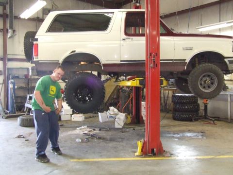 1990 Ford Bronco - A white and maroon Ford Bronco is shown on a vehicle lift in a garage, with a man standing nearby.