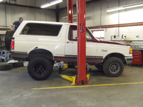 1990 Ford Bronco - A white and maroon Ford Bronco is shown on a lift in a garage, possibly undergoing maintenance.